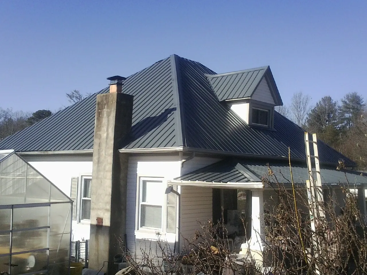 Dark blue standing seam metal roof on a white farmhouse with dormer — Slate & Tile Roof Repair by Roofing Brothers in Hoschton