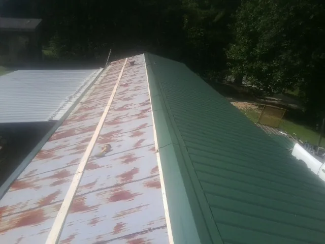 Old rusted panels beside newly installed green metal roofing — Wind Damage Roof Repair by Roofing Brothers in Hoschton