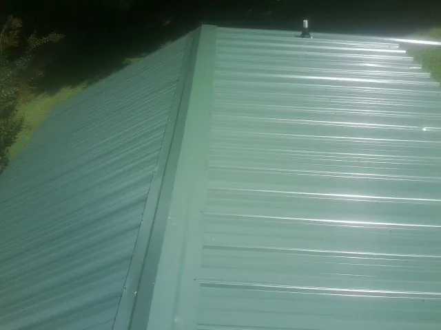 New green metal panels meeting at the ridge of a roof — Flat Roof Repair work by our crew in Hoschton
