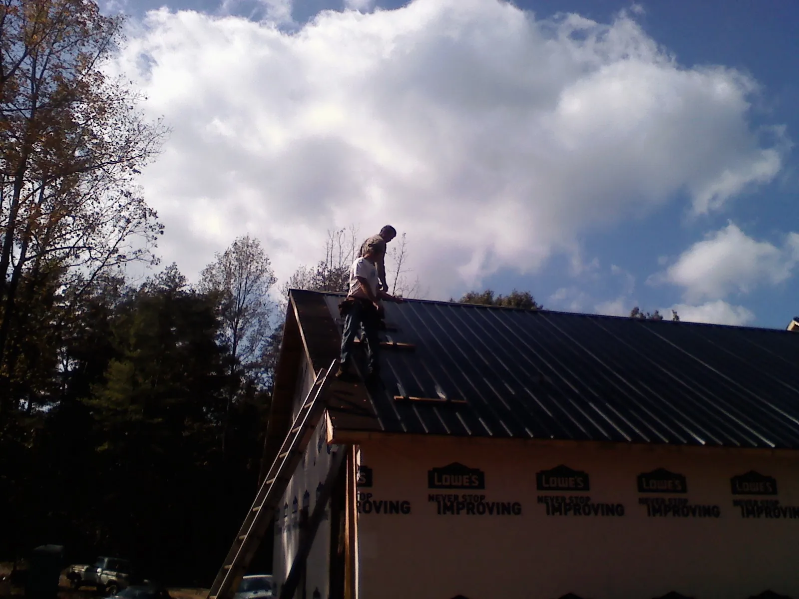 Roofer fastening dark metal panels high against a cloudy sky, from a Roof Inspection job in Hoschton