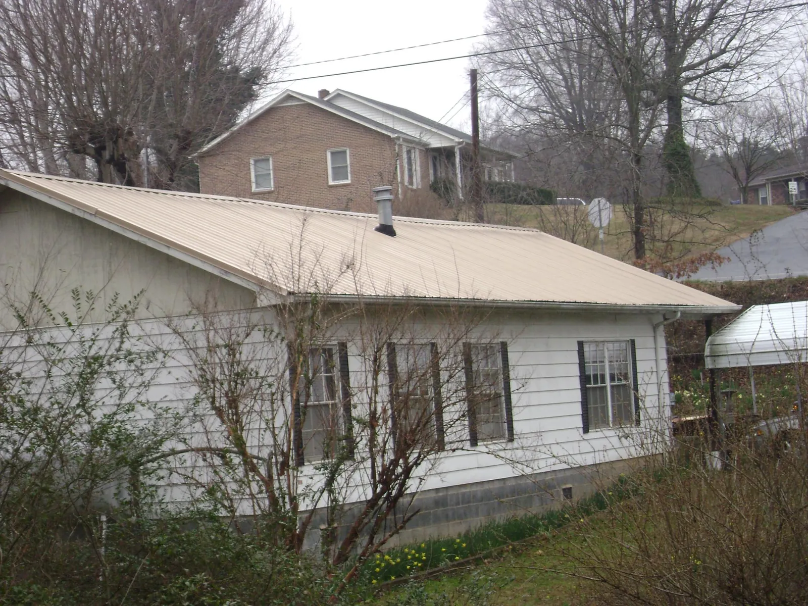 Tan metal roof on a white sided house set into a hillside — Commercial Roofing by Roofing Brothers in Hoschton
