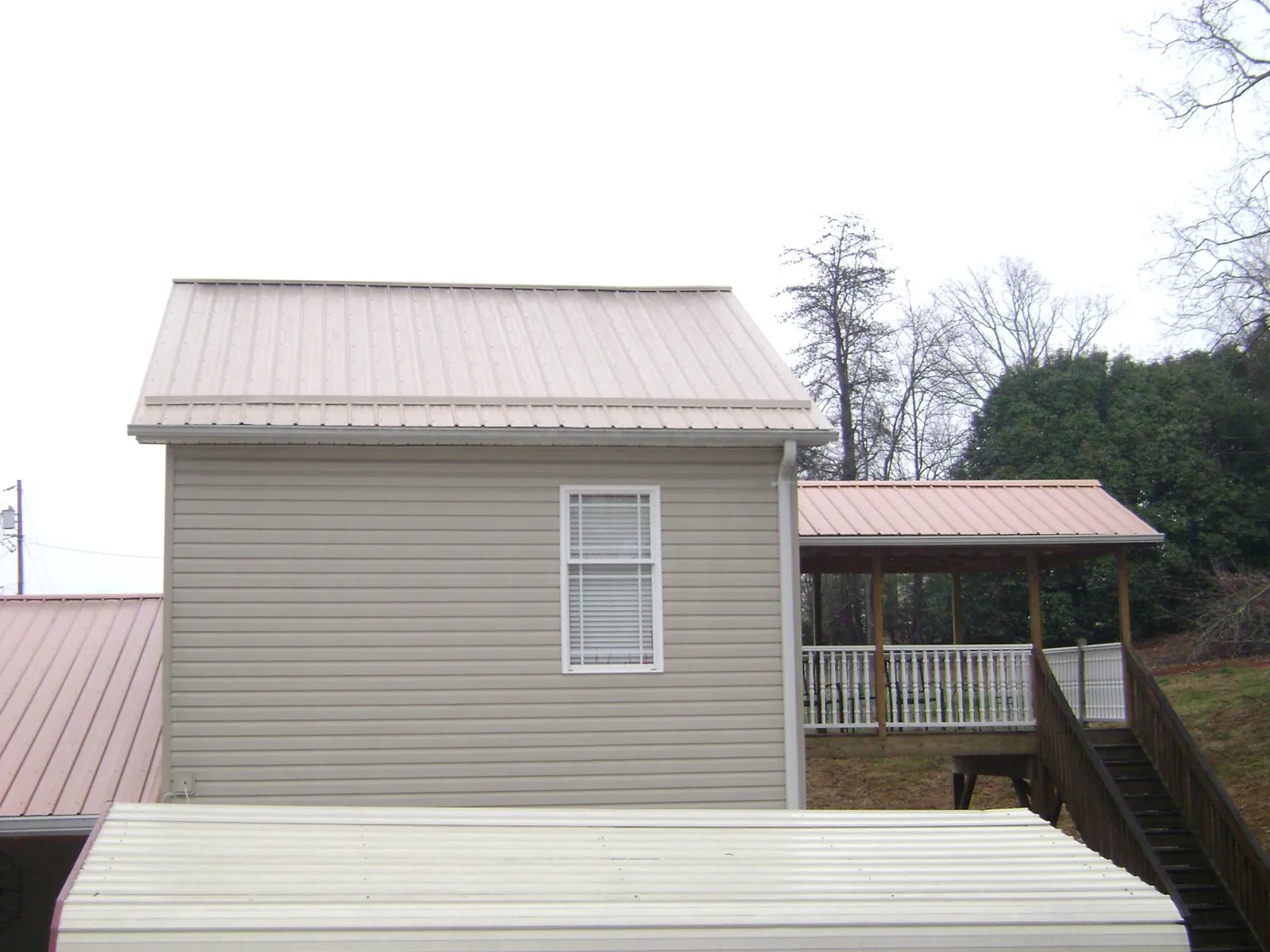 Tan metal roofs on a two story addition and attached porch, from a Roof Replacement job in Hoschton